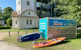 Während sie einen Raum mieten in Konstanz im Wasserturm Stromeyersdorf, empfiehlt sich im Anschluss eine Stand-Up-Paddle-Tour. Blick auf die Stand-Up-Paddle-Verleihstation der Marke Heiuki direkt neben dem Wassertu